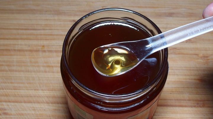 Ein Glas Honig steht auf einem Holztisch, während ein Löffel den goldenen Honig aufnimmt, um Nagelpilz zu bekämpfen.