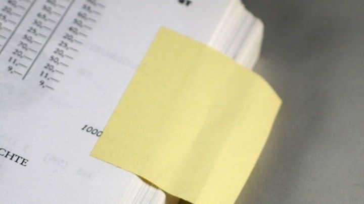 Ein gelber Haftnotizzettel markiert eine bestimmte Seite in einem Buch, um als Lesezeichen zu dienen.