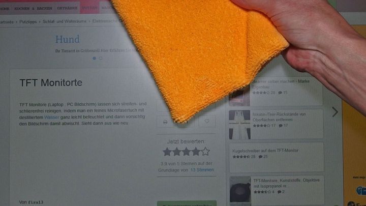 Ein Hand mit einem gelben Tuch wischt &uuml;ber einen TFT Monitor, um ihn streifenfrei zu reinigen.