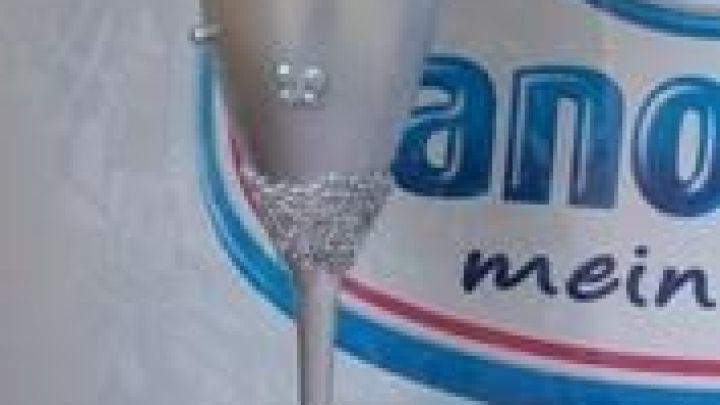 Ein Sektglas mit glitzernden Verzierungen steht dekorativ in einem eleganten Umfeld, geschm&uuml;ckt mit einer Blume oben drauf.