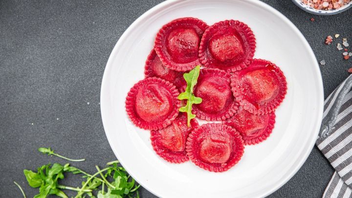 Rote Bete Nudeln liegen ansprechend in einer wei&szlig;en Schale, umgeben von frischen Kr&auml;utern auf dunklem Hintergrund.