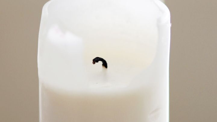 Ein Kerzendocht aus Topflappengarn ragt aus einer wei&szlig;en, brennenden Kerze, die in einem ruhigen Raum steht.