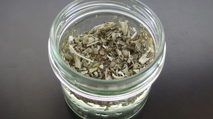 Ein Glas mit trockenen Salbeibl&auml;ttern steht auf einer dunklen Oberfl&auml;che, bereit zur Herstellung von Mundwasser oder Sp&uuml;lung.