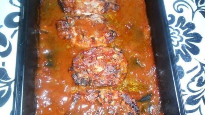 Saftige Koteletts liegen in einer w&uuml;rzigen Sauce auf einem schwarzen Teller, umgeben von einer blumenartigen Tischdecke.