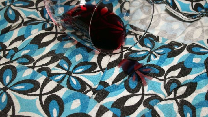 Ein Weinglas ist umgefallen und hinterl&auml;sst Rotweinflecken auf einem bunten Tuch mit floralem Muster.