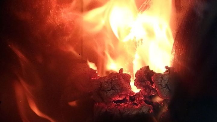 Flammen lodern hell &uuml;ber gl&uuml;henden Grillkohle, w&auml;hrend Salz zur Brandbek&auml;mpfung eingesetzt wird.