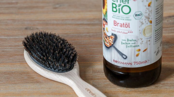 Ein Haarb&uuml;rste liegt neben einer Flasche &Ouml;l auf einem Holztisch, bereit, um Kaugummi aus dem Haar zu entfernen.