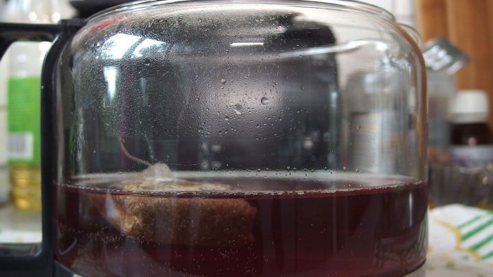 Ein Teebeutel schwebt &uuml;ber einer Kanne mit steigendem, dampfendem Tee, umgeben von einer modernen K&uuml;chenumgebung.