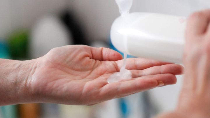 Eine Hand h&auml;lt Shampoo, w&auml;hrend es aus einer Flasche in die Handfl&auml;che flie&szlig;t, bereit zur Anwendung als Duschgel.