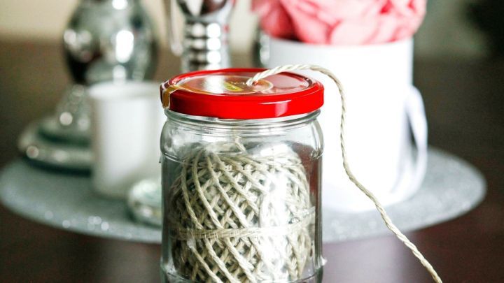 Ein Marmeladenglas mit rotem Deckel enth&auml;lt eine Schnur und Kordel, auf einem dekorativen Tisch mit Kerzen und Blumen.