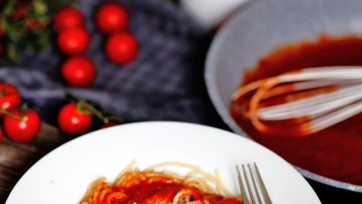 Ein Teller Spaghetti umgeben von frischen Tomaten und einer Sch&uuml;ssel mit roter Tomatencreme auf einem Holztisch.