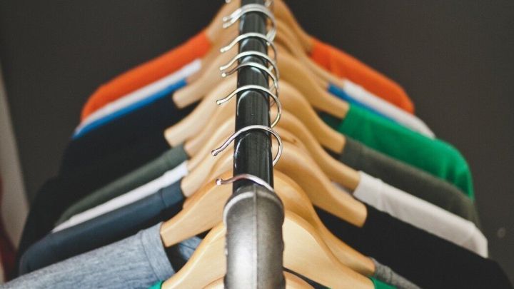 Bunte T-Shirts h&auml;ngen ordentlich an einem Kleiderst&auml;nder, w&auml;hrend ein gro&szlig;er Kalender an der Wand im Hintergrund sichtbar ist.