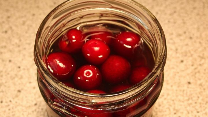 Ein Glas mit roten S&uuml;&szlig;kirschen ist gef&uuml;llt mit einem klaren Fl&uuml;ssigkeitsansatz, wahrscheinlich f&uuml;r das Einwecken.