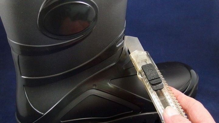 Ein Gummistiefel wird mit einem Cutter bearbeitet, um ihn in einen Gummischuh umzuwandeln. Der Hintergrund ist blau.