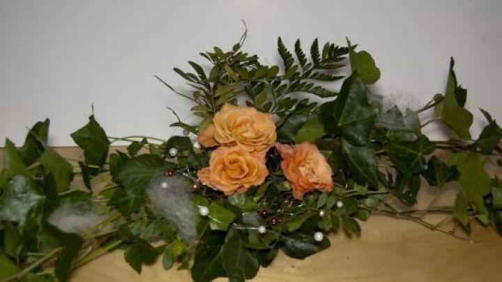 Rosenbl&uuml;ten sind kunstvoll in gr&uuml;nen Bl&auml;ttern und Zweigen arrangiert, ideal f&uuml;r eine elegante Tischdekoration.