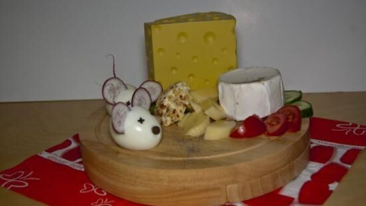 Eine dekorative K&auml;seplatte zeigt aus Eiern gestaltete M&auml;use, umgeben von verschiedenen K&auml;sesorten, Gem&uuml;se und einer roten Serviette.