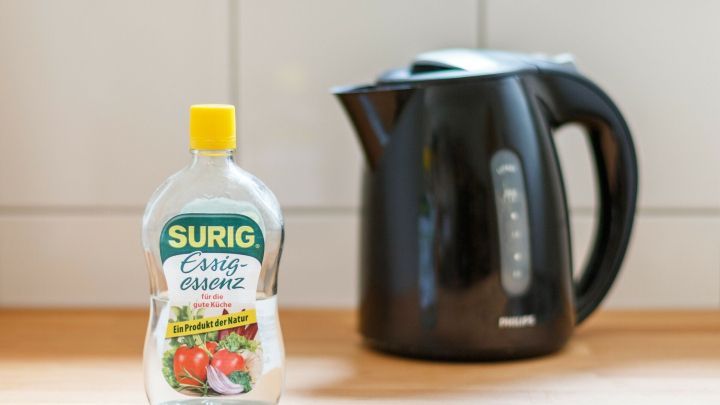 Ein Wasserkocher steht neben einer Flasche Essig auf einer Holzoberfl&auml;che, bereit zum Putzen von Klo und Wasserkocher.