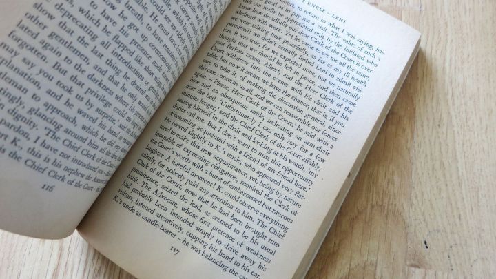 Buch liegt aufgeklappt auf einem Holztisch, Seiten darunter umgebl&auml;ttert. Text zeigt: "K.'s UNCLE...based...Chief...balancing...".