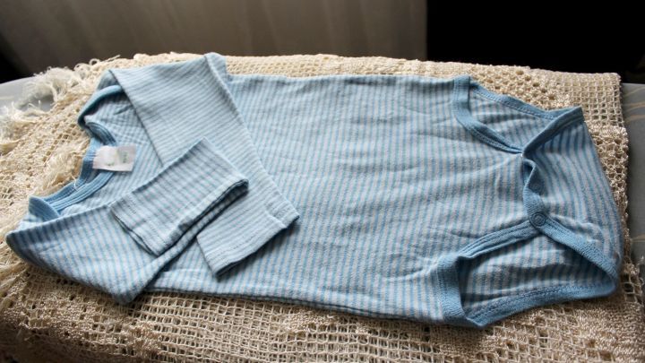Ein blauer Babyanzug liegt auf einem hellen H&auml;kel decke, bereit, mit Kernseife von Flecken befreit zu werden.