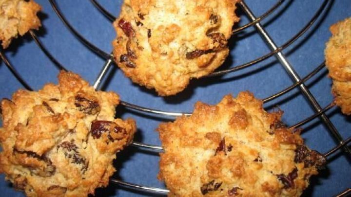 Vollkorn-Makronen mit Cranberries k&uuml;hlen auf einem schwarzen Kuchengitter ab, platziert auf blauem Hintergrund. Kein Text vorhanden.