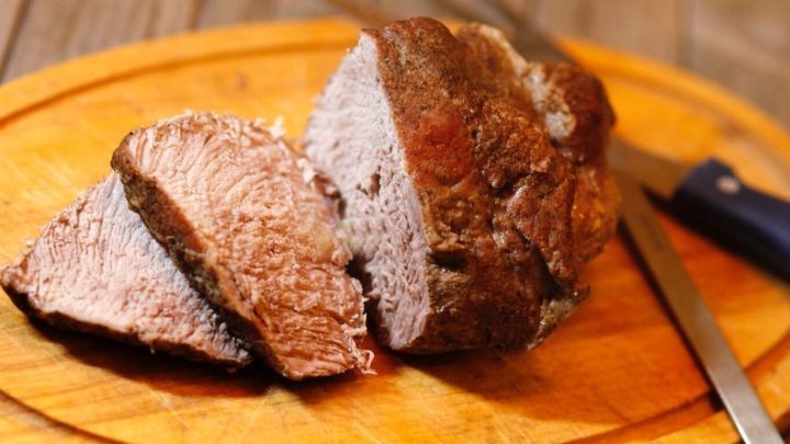 Ein Braten liegt auf einem Holzbrett, w&auml;hrend ein Teil bereits in Scheiben geschnitten ist, um ihn zu servieren.