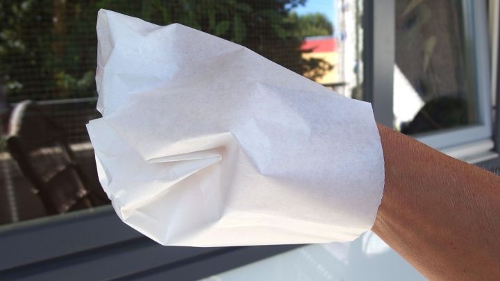 Eine Hand tr&auml;gt einen zerknautschten Butterbrotbeutel und reinigt damit ein Fenster im Freien.