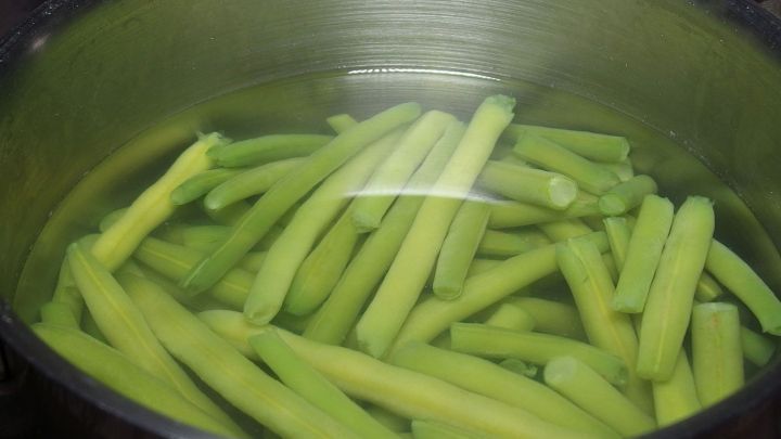 Gr&uuml;ne Gem&uuml;sest&auml;ngel schwimmen in einem Topf mit Wasser, bereit zum Kochen, um die Farbstabilit&auml;t durch Kaiser Natron zu erhalten.