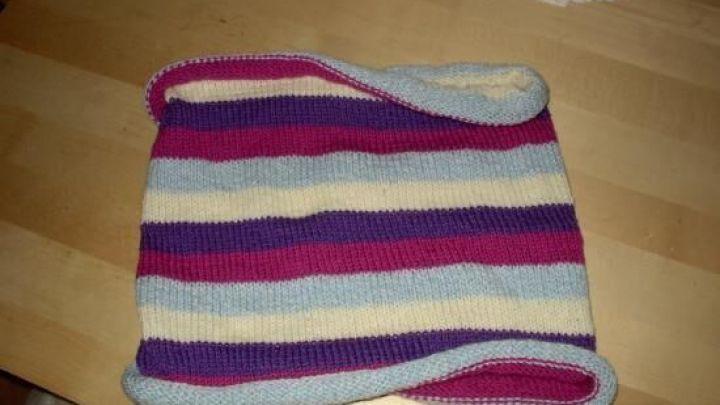 Ein gestricktes, bunt gestreiftes St&uuml;ck liegt flach auf einem Holztisch.
