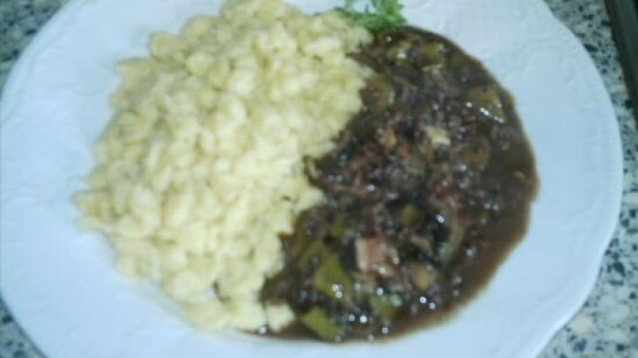 Ein Teller mit Ragout de boeuf hach&eacute; au vin rouge, serviert mit Sp&auml;tzle, auf einer wei&szlig;en Unterlage in einer K&uuml;che.