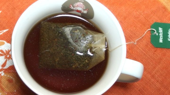 Eine Tasse mit dampfendem Kr&auml;utertee zieht einen Teebeutel auf einem orangefarbenen Tischcloth.