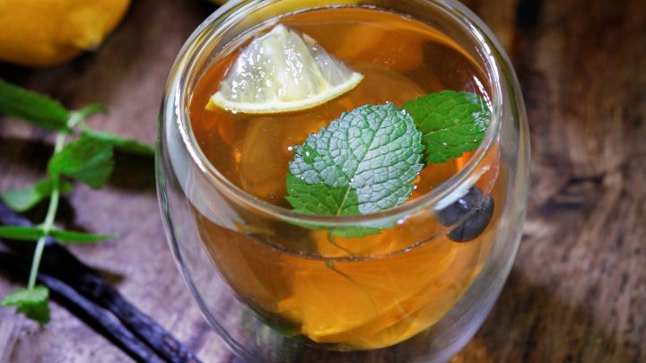 Ein Glas Tee mit Zitrone und Minze steht auf einem Holzuntergrund, umgeben von Zitronen und Vanilleschoten.