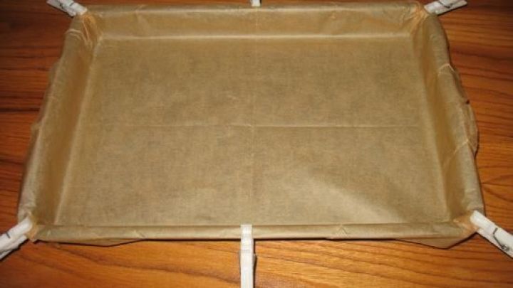 Ein Backblech ist mit Backpapier ausgelegt und auf einem Holzuntergrund positioniert, bereit f&uuml;r das Backen.