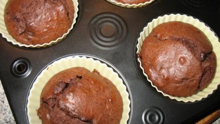 Schoko-Muffins backen im schwarzen Muffinblech auf einer K&uuml;chenarbeitsplatte.