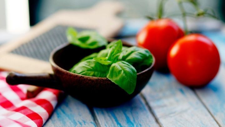 Ein Holzsch&auml;lchen mit frischem Basilikum steht neben roten Tomaten auf einem Tisch, ideal f&uuml;r &Auml;therisches Basilikum&ouml;l.