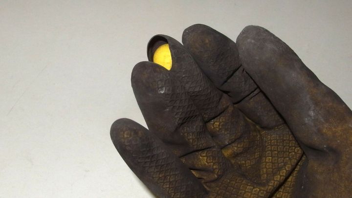 Ein abgenutzter, schmutziger Gartengummihandschuh zeigt ein Loch auf, w&auml;hrend er eine kleine gelbe Pflanze h&auml;lt.