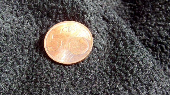 Ein Kupferst&uuml;ck liegt auf einem dunklen, strukturierten Stoff, der einen Kontrast zu seiner gl&auml;nzenden Oberfl&auml;che bietet.