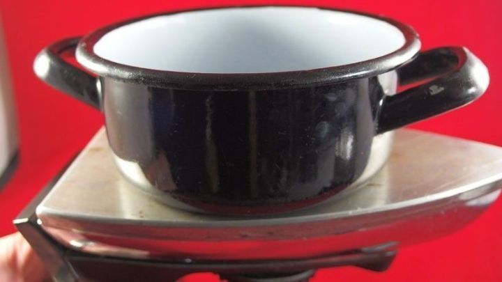 Ein B&uuml;geleisen wird als Kochplatte genutzt, w&auml;hrend ein kleiner schwarzer Topf darauf steht. Der Hintergrund ist rot.