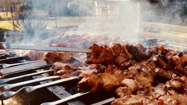 Saftige Schaschlikspie&szlig;e grillen &uuml;ber gl&uuml;henden Kohlen, w&auml;hrend Rauch fr&ouml;hlich in einem sonnigen Garten aufsteigt.