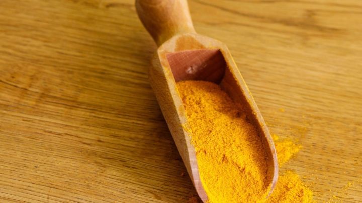 Ein Holzl&ouml;ffel mit Kurkumapulver auf einer Holzoberfl&auml;che, das f&uuml;r die Linderung von Schmerzen nach einer H&auml;morrhoiden-OP verwendet wird.