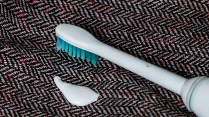 Eine elektrische Zahnb&uuml;rste liegt neben einem Zahnpastafleck auf einem gestreiften Stoff. Der Fleck deutet auf Reinigung hin.