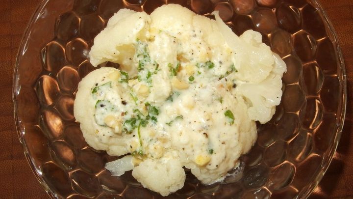 Ein Blumenkohlsalat wird in einer durchsichtigen Sch&uuml;ssel serviert, umgeben von einer rustikalen Tischumgebung.