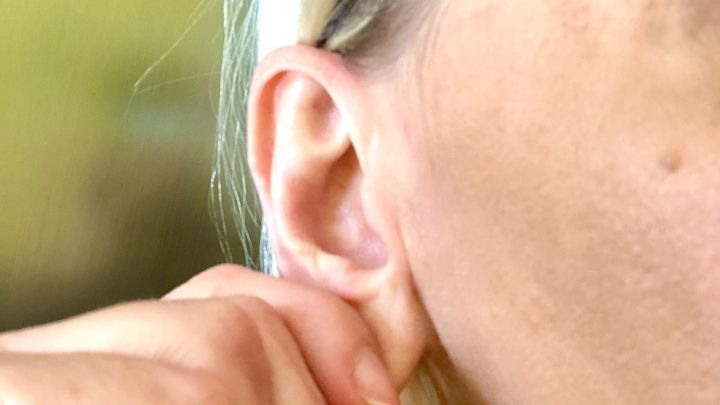 Eine Hand greift an das Ohr einer Person, um zu helfen, Wasser im Ohr zu entfernen. Der Hintergrund ist unscharf.