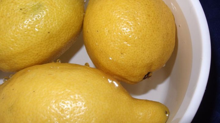 Drei frische Zitronen liegen in einer Sch&uuml;ssel mit Wasser, um sie haltbarer zu machen. Sie sind intensiv gelb und gl&auml;nzend.