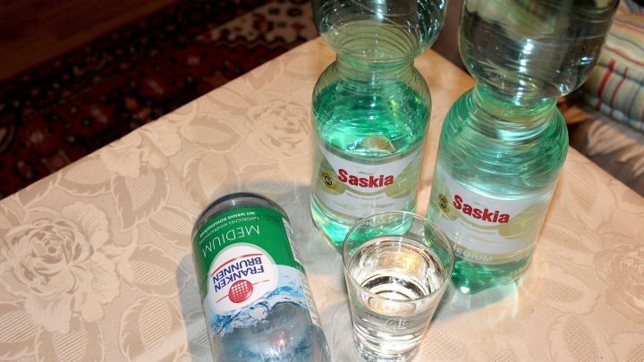 Flaschen mit Wasser stehen auf einem Tisch, w&auml;hrend ein Glas gef&uuml;llt wird &ndash; erfrischende Getr&auml;nke ohne K&uuml;hlschrank.