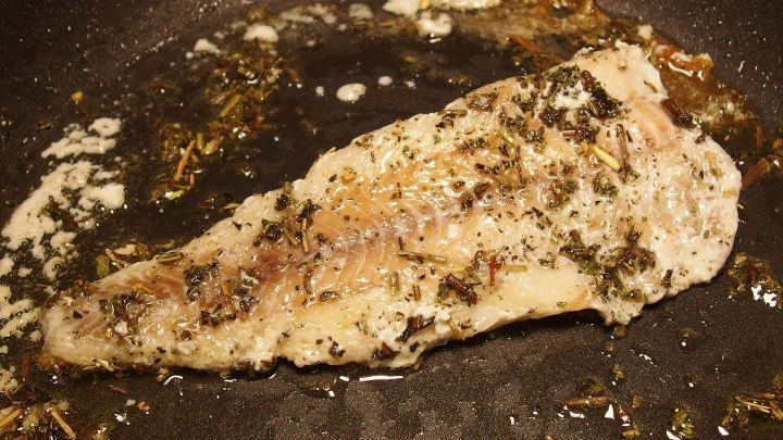 Ein Fischfilet br&auml;t in einer Pfanne, w&auml;hrend der Kochgeruch den Raum erf&uuml;llt und sich mit anderen Aromen vermischt.
