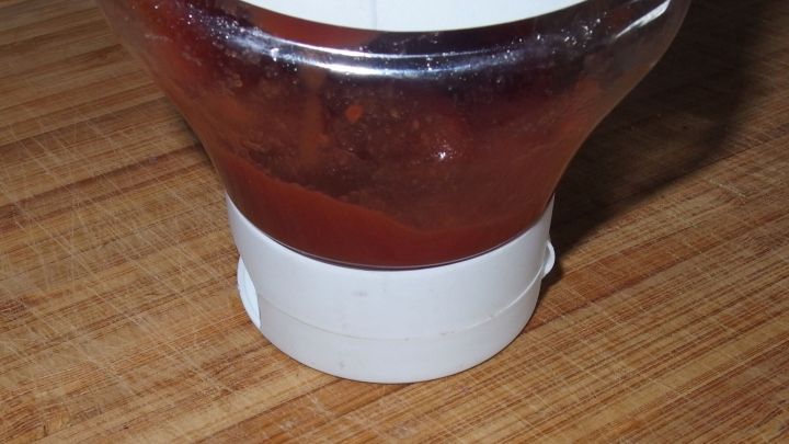 Ein Ketchupbeh&auml;lter steht auf einem Holztisch, der letzte Rest Ketchup wird sichtbar, w&auml;hrend die Flasche kaum gef&uuml;llt ist.