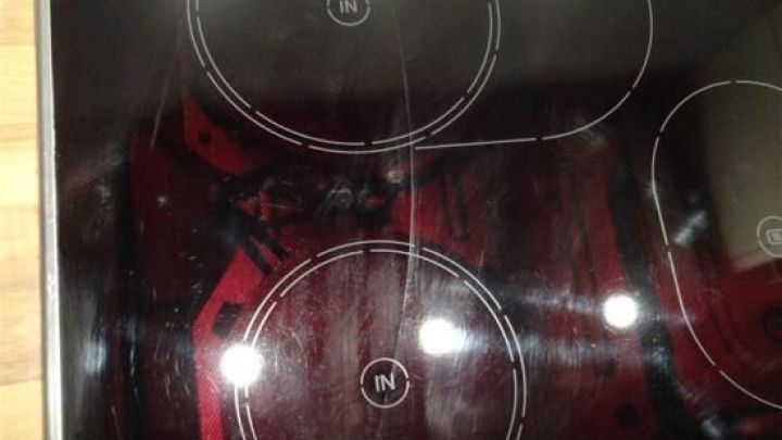 Ein Glaskeramikfeld liegt auf einem Holzfu&szlig;boden und zeigt Kratzer auf der Oberfl&auml;che, bereit zum Ausbauen oder Wechseln.