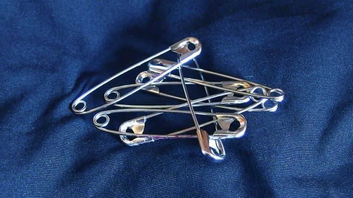 Eine Gruppe von Sicherheitsnadeln liegt gesammelt auf einem blauen Laken, bereit, um das Lakenwirrwarr zu l&ouml;sen.