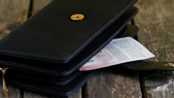 Eine schwarze Geldb&ouml;rse liegt auf einem Holztisch, teilweise ge&ouml;ffnet, zeigt eine Sonnenmilch-Probe und einen Zettel.