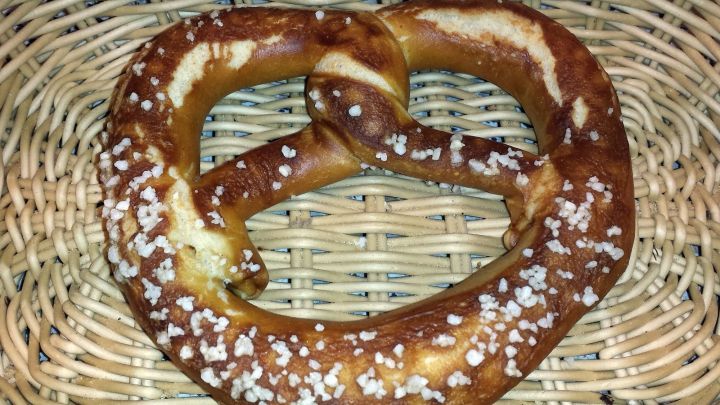 Eine frische Brezel mit Salz liegt auf einem geflochtenen Korb, umgeben von einem rustikalen Ambiente, die perfekte Snack-Option.